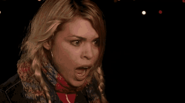 a woman wearing a scarf and a denim jacket looks surprised