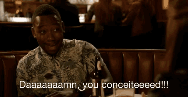 a man sits at a table with a bottle of beer and says " daaaaamn you conceiteeed "
