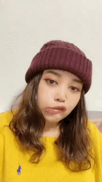 a woman wearing a purple hat and a yellow sweater is making a face .