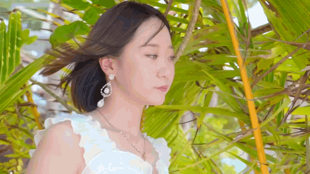 a woman in a white dress and earrings is standing in front of palm trees .