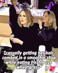 a woman is getting her hair combed in a smoothie shop while eating freshly cut wheatgrass .