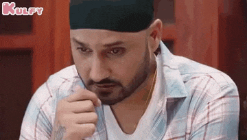 a man wearing a turban and a plaid shirt is sitting at a table with his hand on his chin .