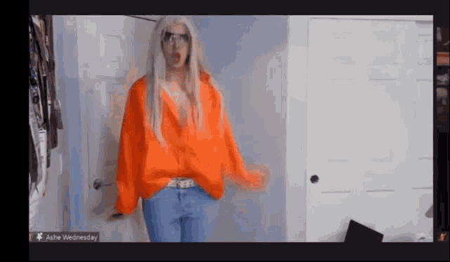 a woman in an orange shirt and blue jeans is standing in front of a door