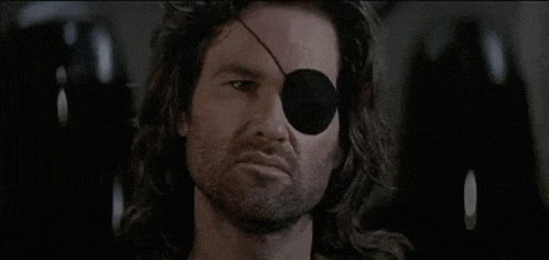 a man with long hair and a black eye patch looks at the camera