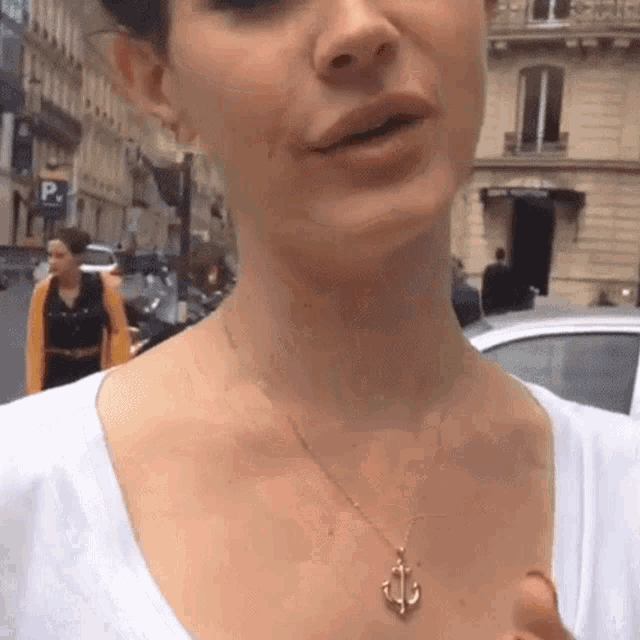 a woman wearing a necklace with an anchor on it stands in front of a parking sign
