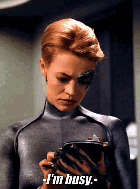 a woman in a black suit is holding a cell phone and says i 'm busy
