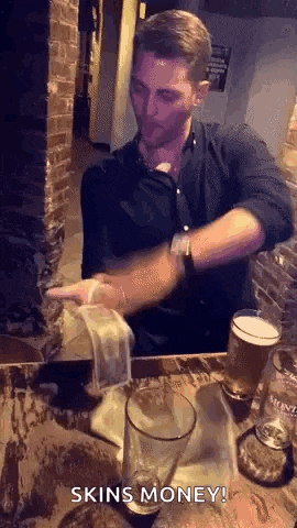 a man is sitting at a table with a glass of beer and a stack of money .