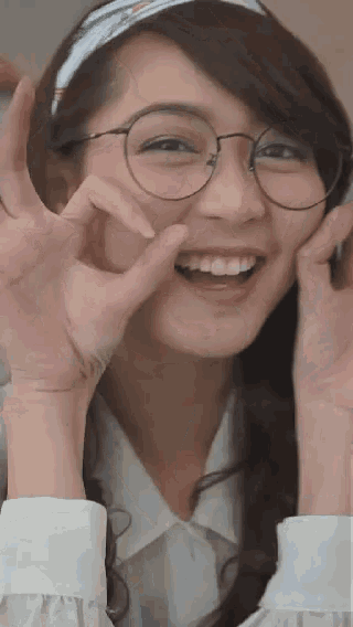 a woman wearing glasses and a headband is smiling and making a peace sign with her hands