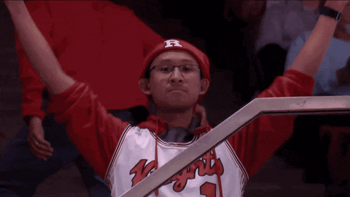 a man wearing a red hat with the letter r on it stands with his arms in the air