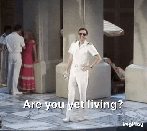 a man in a white suit is standing in front of a group of people and says are you yet living