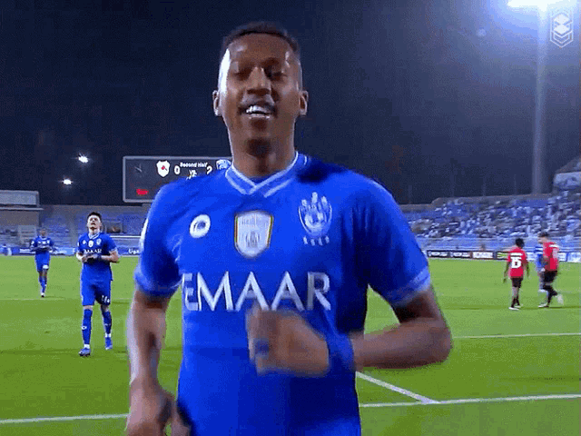 a soccer player wearing a blue emaar jersey runs on the field