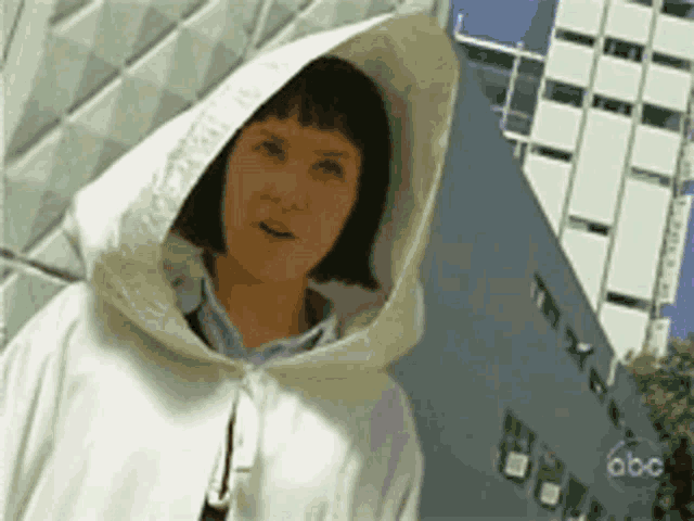 a woman wearing a white hooded jacket is standing in front of a building that says abc on it