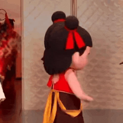 a doll with a red bow in her hair is standing in front of a mirror .