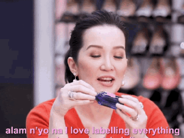 a woman in a red shirt is holding a small object and says alam nyo na love labelling everything