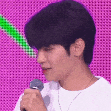 a young man is holding a microphone in front of a pink and green background .