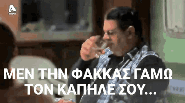 a man sitting on a couch drinking from a glass with greek writing on the screen