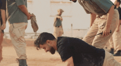 a man in a black shirt is kneeling on the ground while another man stands behind him