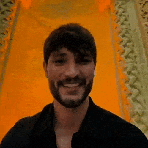 a man with a beard and mustache is smiling in front of a yellow wall .