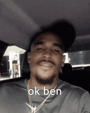 a man wearing a hat and a necklace is sitting in a car with the words ok ben above him