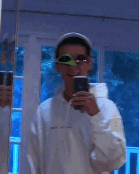 a man wearing sunglasses and a hat is taking a selfie in a mirror