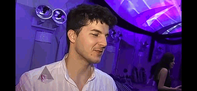a man in a white shirt is standing in a room with purple lights behind him .