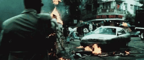 a man stands in front of a burning car in front of a building that says beer hall