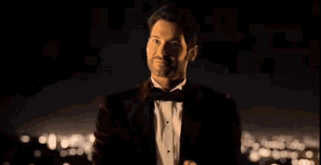 a man in a tuxedo is standing on a balcony overlooking the city at night