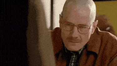 a bald man wearing glasses and a brown jacket is looking at a woman .