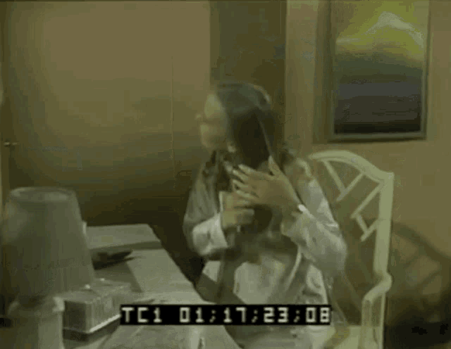 a woman sits at a desk with a tc1 01 : 17 : 25 : 23 time stamp