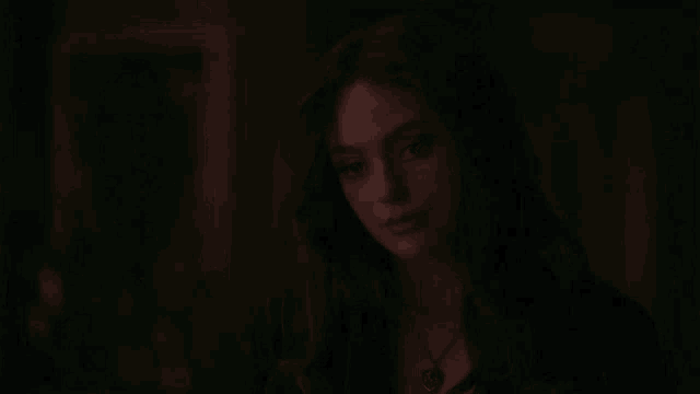 a close up of a woman 's face in a dark room with a painting in the background .