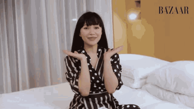 a woman in a black and white polka dot dress sits on a bed
