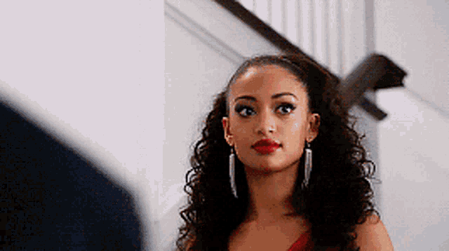 a woman in a red dress and earrings is standing in front of stairs .