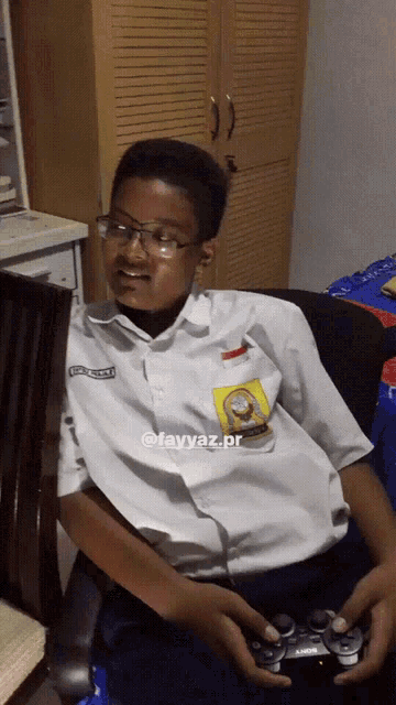 a boy in a school uniform is playing a video game with a playstation controller