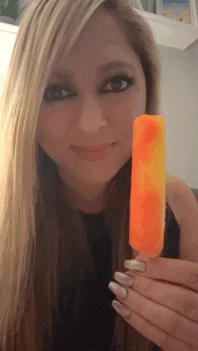 a woman is holding an orange and yellow popsicle in front of her face