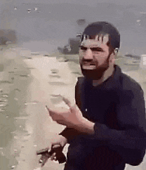 a man with a beard is holding a gun while standing on a beach .