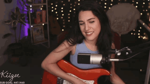 a woman playing a guitar in front of a microphone with the name kiiger on the bottom left