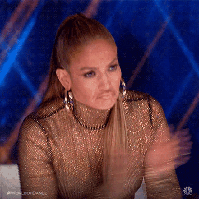 a woman in a gold dress is clapping her hands while wearing hoop earrings .