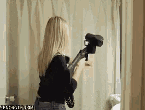 a woman is holding a camera that looks like a gun in a bathroom .