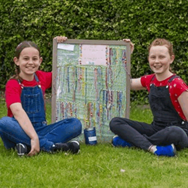 two young girls are sitting on the grass holding a framed picture