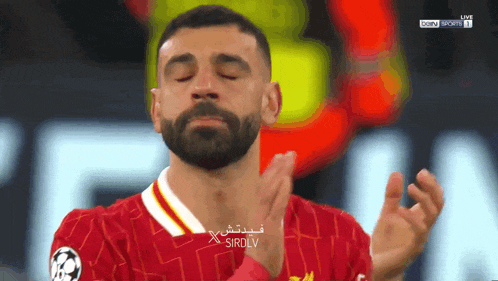 a man with a beard applauds while wearing a red shirt that says sirdlv on it