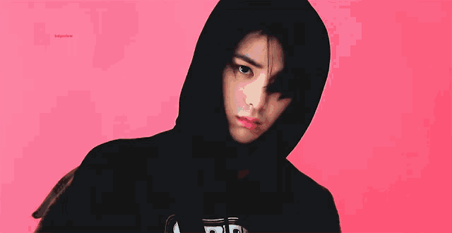 a person wearing a black hoodie with a pink background .
