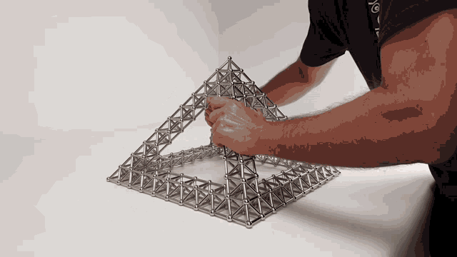a man in a blue shirt is working on a pyramid made out of magnets