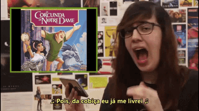 a girl with glasses is holding a cell phone in front of a poster for corcunda de notre dame