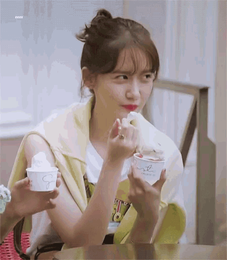 a woman is sitting at a table eating ice cream from a cup .