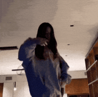 a woman is dancing in a room with a ceiling fan and she is wearing a white sweater .