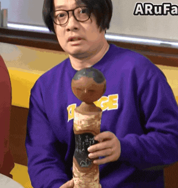 a man in a purple sweatshirt holds a statue in front of a sign that says arufa