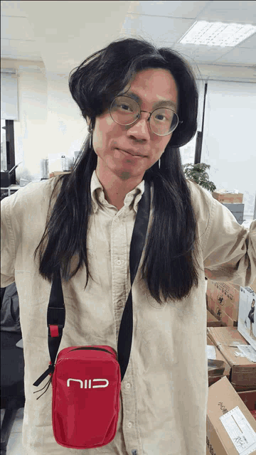 a man with long hair is wearing glasses and carrying a red bag that says cili