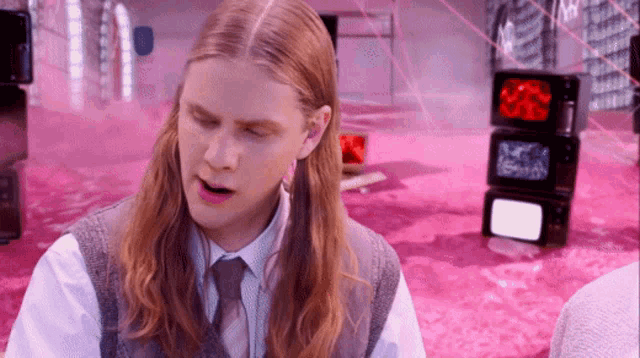 a man with long hair is sitting in front of a stack of tvs