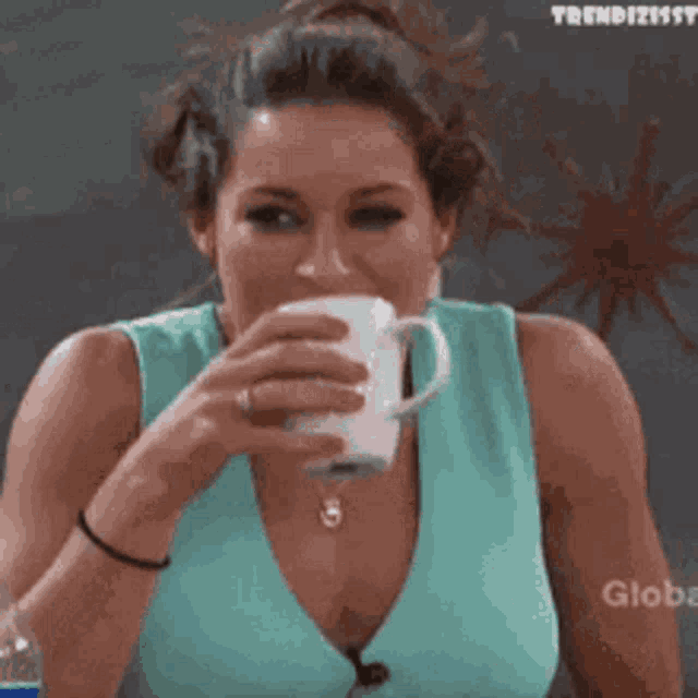 a woman in a blue top is drinking from a white cup .