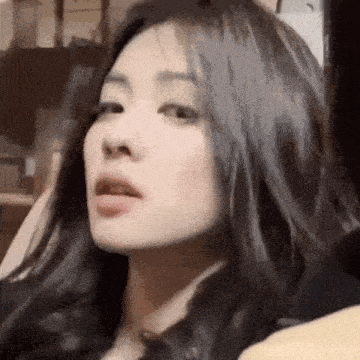 a close up of a woman 's face with long black hair and a surprised look on her face .